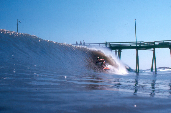 A surfer catches a wave near a pier